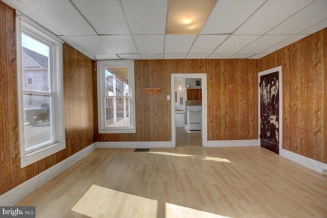 unfurnished room with a drop ceiling, wooden walls, and light hardwood / wood-style floors