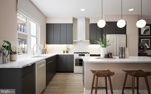 kitchen with stainless steel appliances, sink, decorative light fixtures, wall chimney range hood, and light wood-type flooring