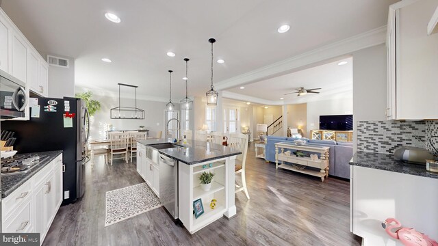 kitchen with white cabinets, appliances with stainless steel finishes, hanging light fixtures, and a center island with sink