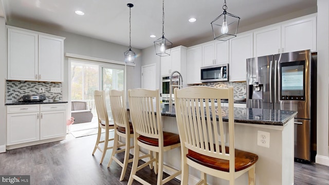 kitchen featuring a kitchen island with sink, appliances with stainless steel finishes, white cabinetry, and decorative light fixtures