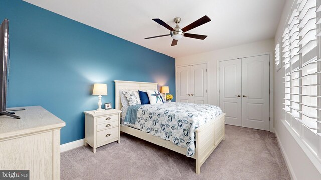 bedroom featuring ceiling fan, light carpet, and two closets