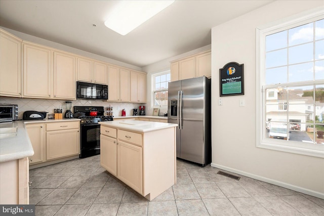 kitchen with black appliances, light tile patterned floors, decorative backsplash, cream cabinetry, and a center island