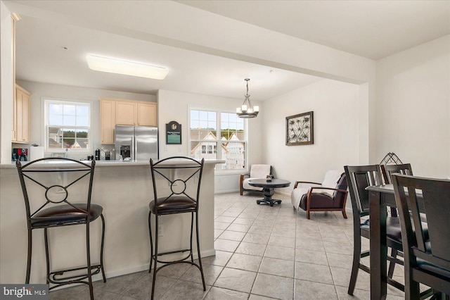 kitchen featuring light tile patterned floors, a kitchen breakfast bar, a notable chandelier, and stainless steel fridge