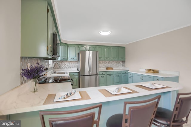 kitchen with kitchen peninsula, tasteful backsplash, a kitchen bar, green cabinetry, and stainless steel fridge