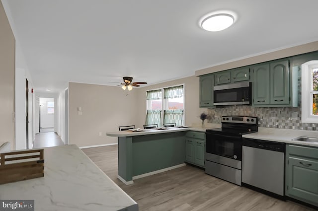 kitchen with green cabinetry, appliances with stainless steel finishes, kitchen peninsula, and light hardwood / wood-style floors