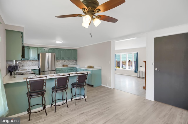 kitchen featuring stainless steel refrigerator, sink, kitchen peninsula, a kitchen bar, and light wood-type flooring