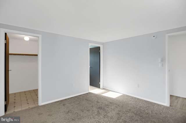 unfurnished bedroom featuring light carpet, a walk in closet, and a closet