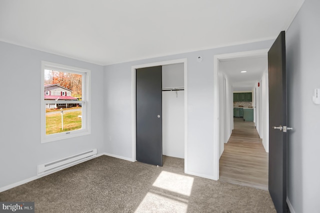 unfurnished bedroom featuring a closet, light hardwood / wood-style floors, and a baseboard heating unit