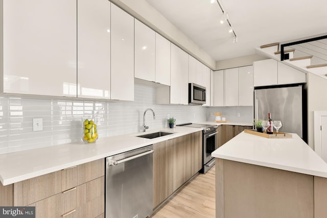 kitchen featuring stainless steel appliances, light wood-type flooring, white cabinetry, sink, and a center island