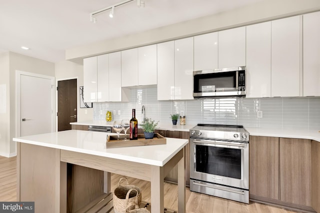 kitchen with white cabinetry, appliances with stainless steel finishes, backsplash, and light wood-type flooring