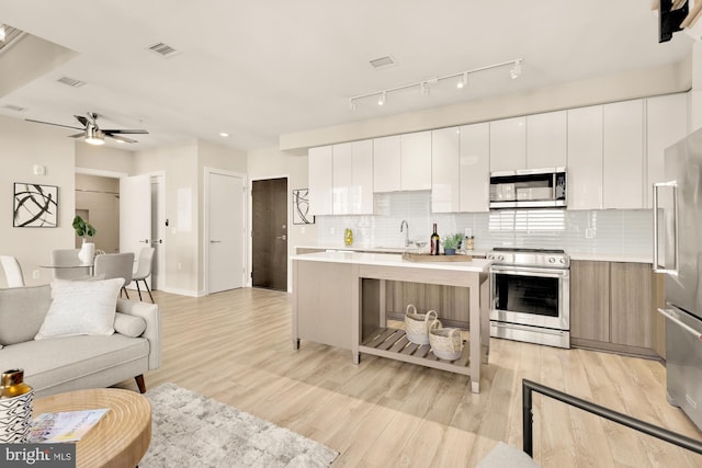 kitchen with tasteful backsplash, a kitchen island, white cabinetry, light wood-type flooring, and appliances with stainless steel finishes