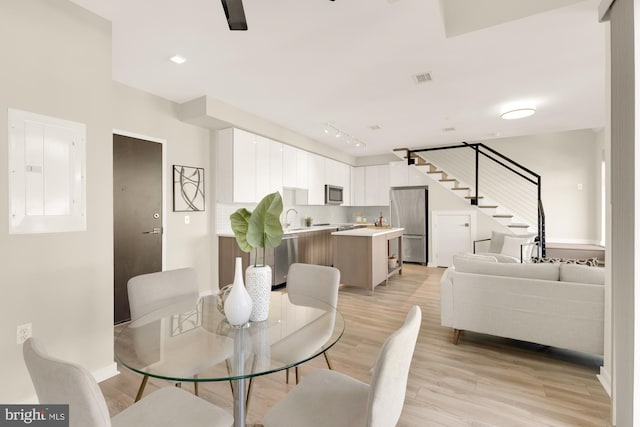 dining space with electric panel, sink, and light wood-type flooring