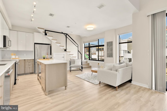 kitchen with stainless steel appliances, a center island, decorative backsplash, white cabinets, and light hardwood / wood-style flooring