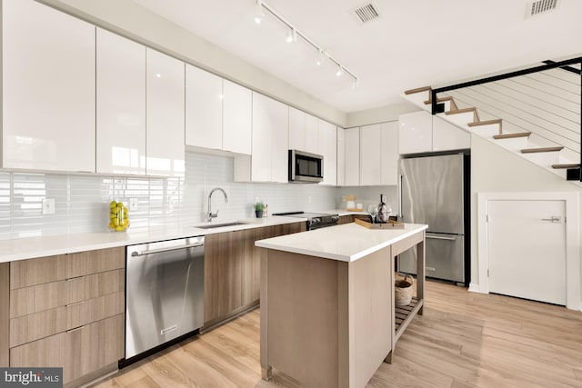 kitchen with stainless steel appliances, light wood-type flooring, white cabinetry, sink, and a center island