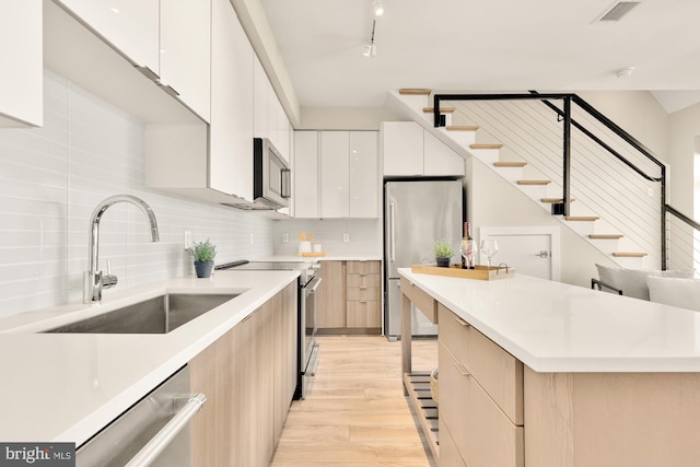 kitchen with stainless steel appliances, white cabinets, sink, tasteful backsplash, and light wood-type flooring