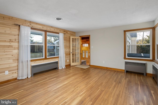 unfurnished living room with radiator, wood walls, and light wood-type flooring