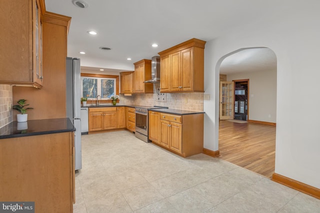 kitchen featuring stainless steel appliances, decorative backsplash, wall chimney range hood, and sink