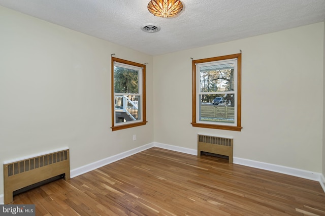 unfurnished room with a textured ceiling, radiator, and hardwood / wood-style floors