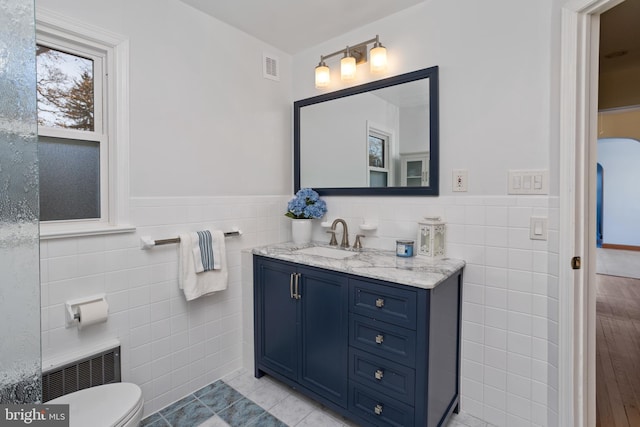 bathroom featuring toilet, tile walls, tile patterned floors, radiator heating unit, and vanity