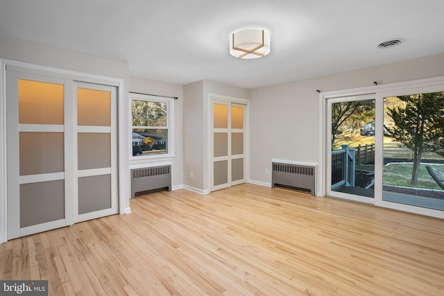 empty room with radiator heating unit, a wealth of natural light, and light hardwood / wood-style floors