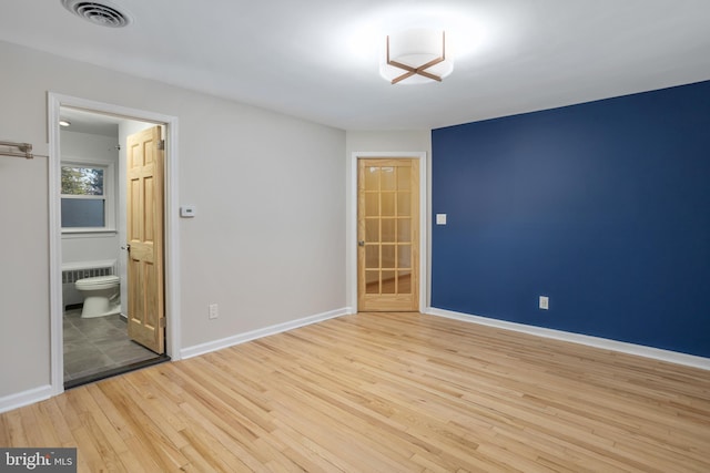 unfurnished bedroom with light wood-type flooring, radiator heating unit, and connected bathroom