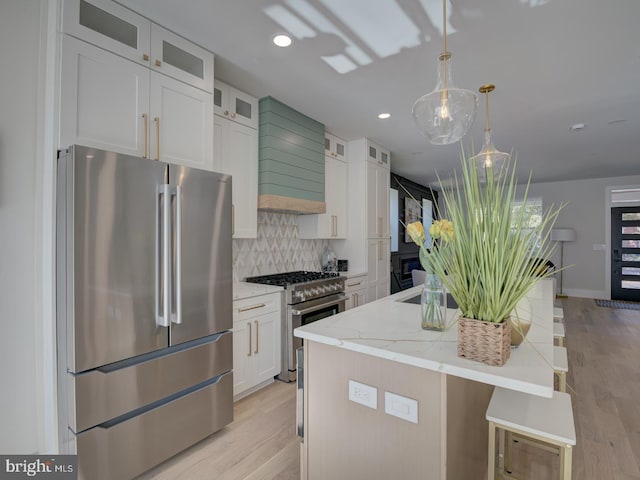 kitchen featuring light hardwood / wood-style floors, an island with sink, white cabinets, premium appliances, and pendant lighting