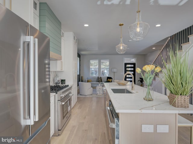 kitchen featuring light hardwood / wood-style floors, premium appliances, a center island with sink, white cabinets, and decorative light fixtures