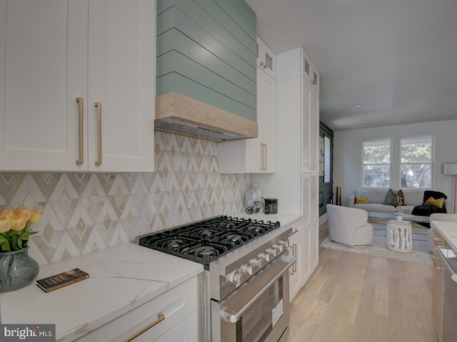 kitchen featuring white cabinetry, light stone countertops, custom range hood, high end stainless steel range, and light wood-type flooring