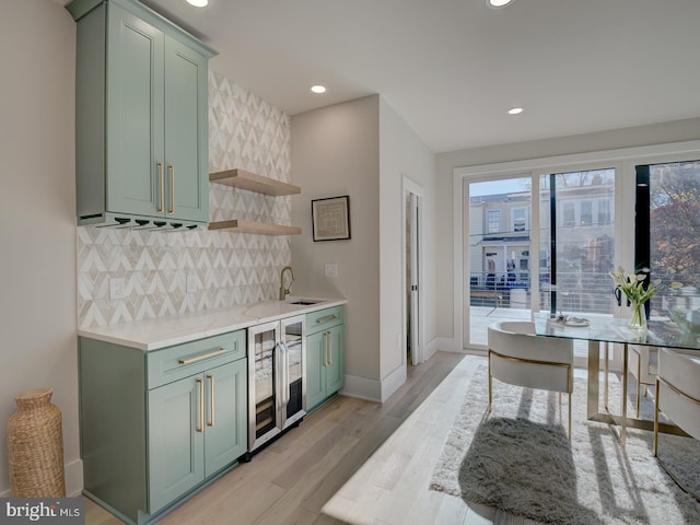 kitchen with backsplash, light wood-type flooring, green cabinetry, sink, and beverage cooler