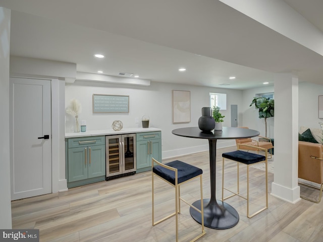 bar featuring beverage cooler, green cabinets, and light wood-type flooring