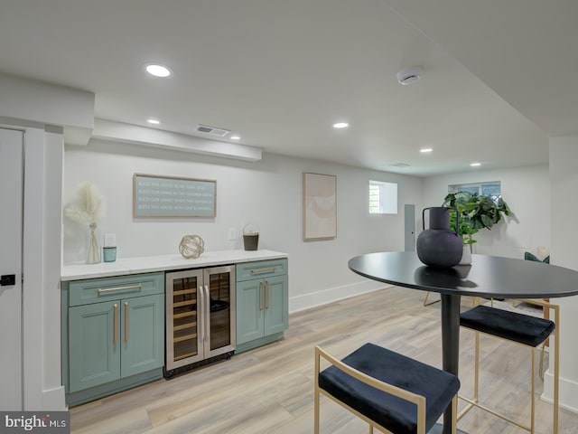 bar featuring green cabinetry, light hardwood / wood-style floors, and beverage cooler