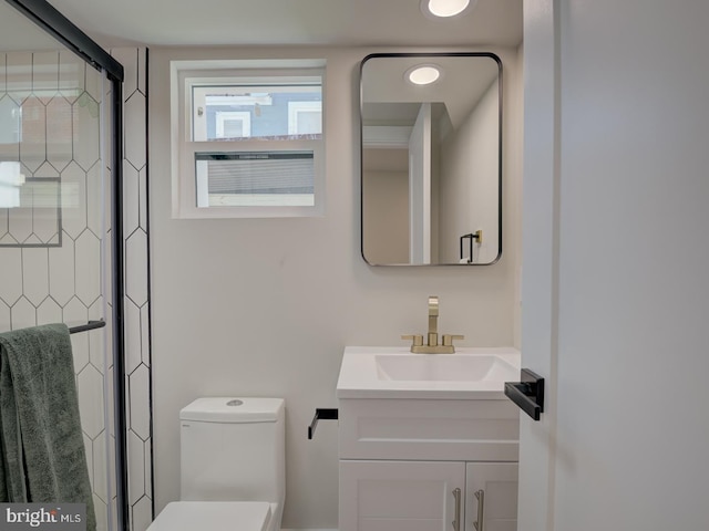 bathroom featuring a shower with door, vanity, and toilet