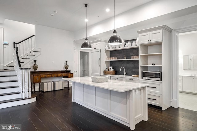 kitchen with stainless steel microwave, white cabinets, hanging light fixtures, light stone countertops, and dark hardwood / wood-style flooring