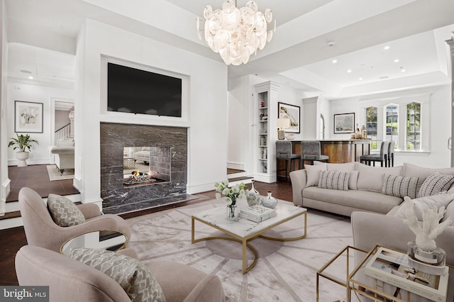 living room featuring a premium fireplace, a raised ceiling, wood-type flooring, and an inviting chandelier