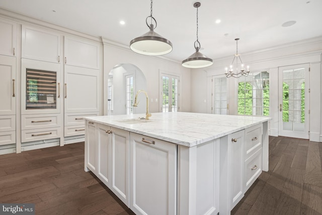 kitchen with dark wood-type flooring, sink, an island with sink, light stone counters, and white cabinetry