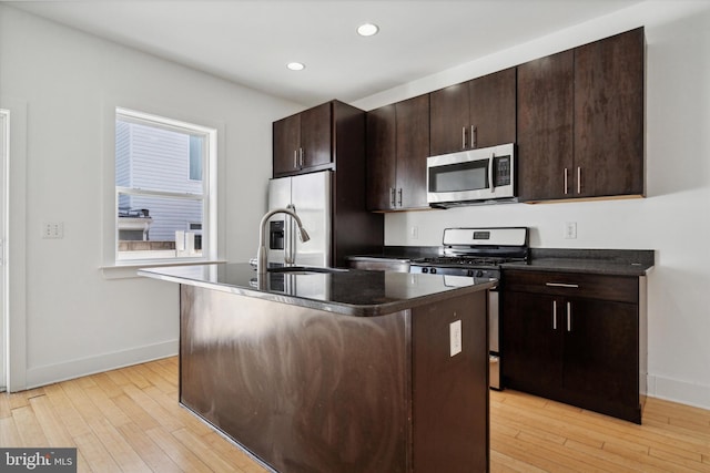 kitchen featuring appliances with stainless steel finishes, dark brown cabinetry, sink, an island with sink, and light hardwood / wood-style floors