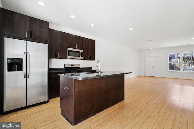 kitchen featuring a center island with sink, stainless steel appliances, dark brown cabinets, sink, and light hardwood / wood-style flooring