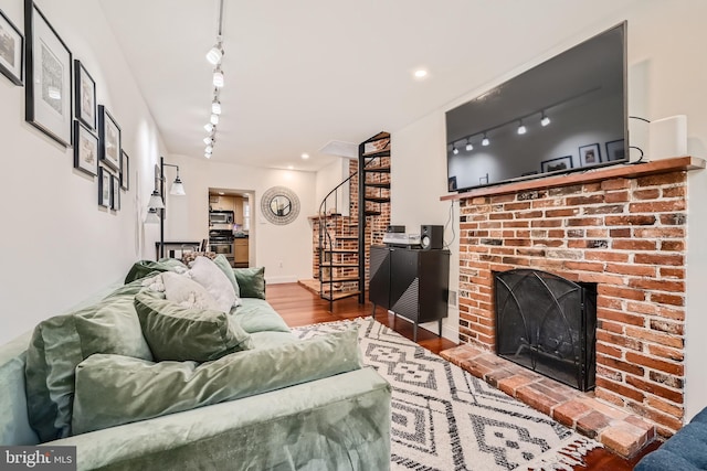 living room featuring hardwood / wood-style floors, track lighting, and a brick fireplace