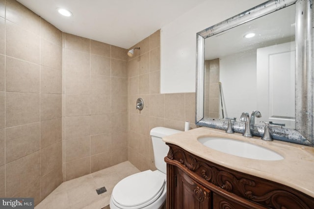 bathroom featuring vanity, toilet, tiled shower, and tile walls