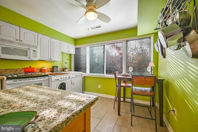 kitchen featuring ceiling fan, light stone countertops, white cabinetry, gas range oven, and independent washer and dryer