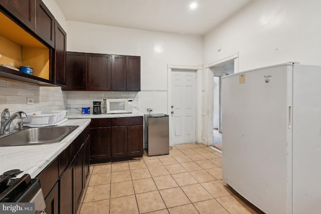 kitchen featuring dark brown cabinetry, white appliances, light tile patterned floors, and sink