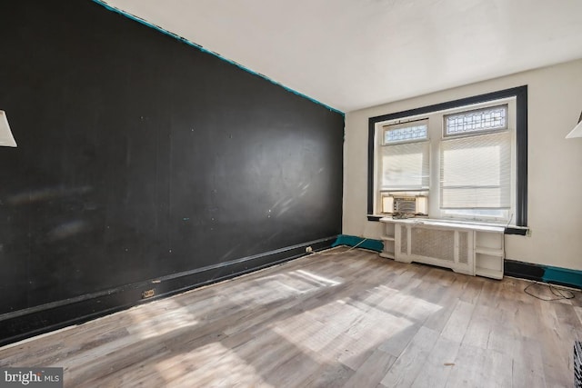 unfurnished room with light wood-type flooring, cooling unit, lofted ceiling, and radiator