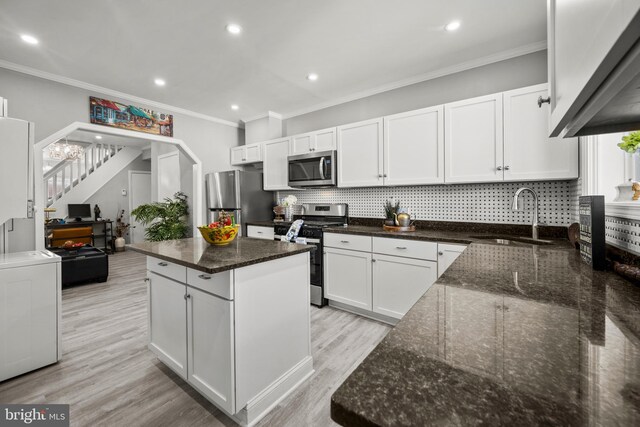 kitchen with dark stone counters, appliances with stainless steel finishes, sink, white cabinets, and a center island