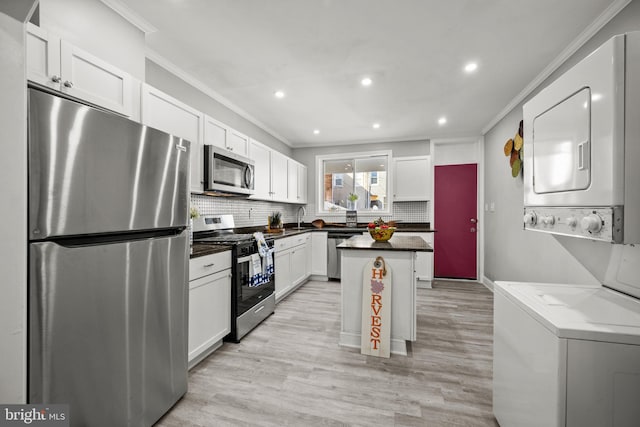 kitchen featuring stainless steel appliances, stacked washer / dryer, a kitchen island, white cabinets, and light wood-type flooring