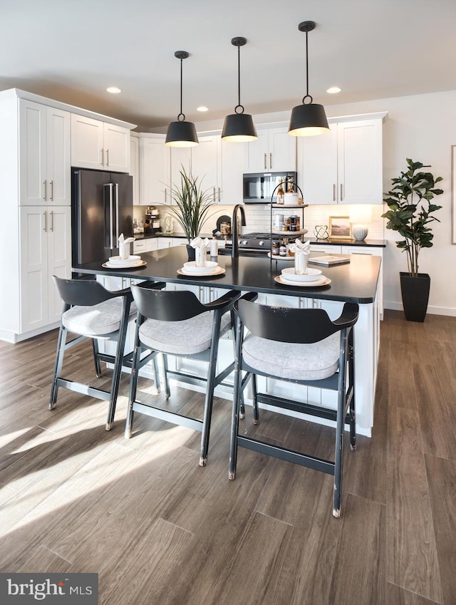 kitchen with white cabinetry, appliances with stainless steel finishes, dark hardwood / wood-style floors, and an island with sink