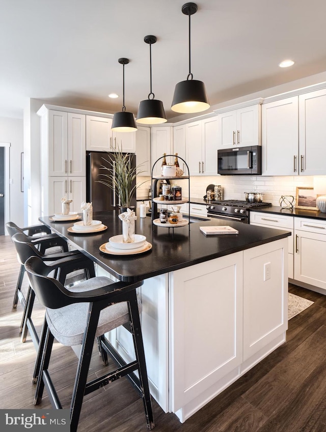 kitchen featuring white cabinets, hanging light fixtures, gas stove, dark hardwood / wood-style floors, and stainless steel fridge