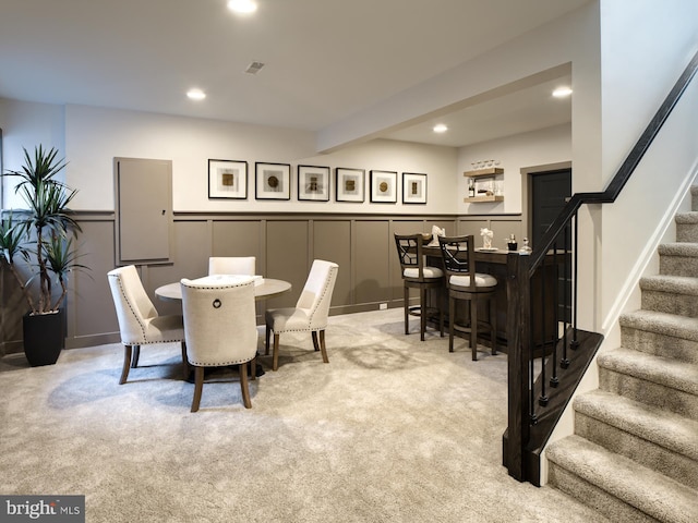 dining area with light colored carpet, beam ceiling, and bar area