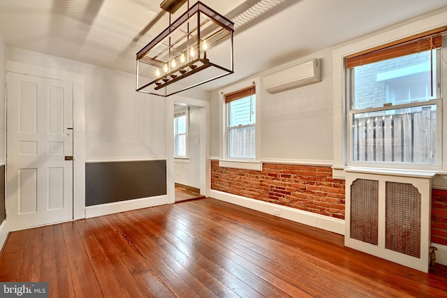 spare room with hardwood / wood-style floors, radiator, a wall mounted AC, and brick wall