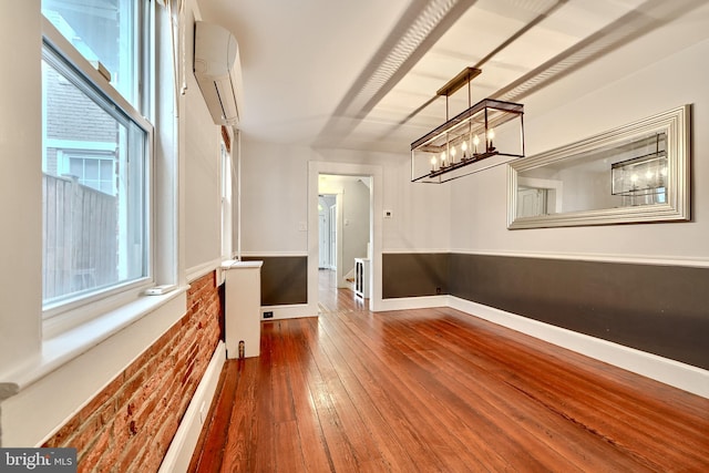 interior space with hardwood / wood-style flooring, brick wall, a healthy amount of sunlight, and a wall mounted air conditioner