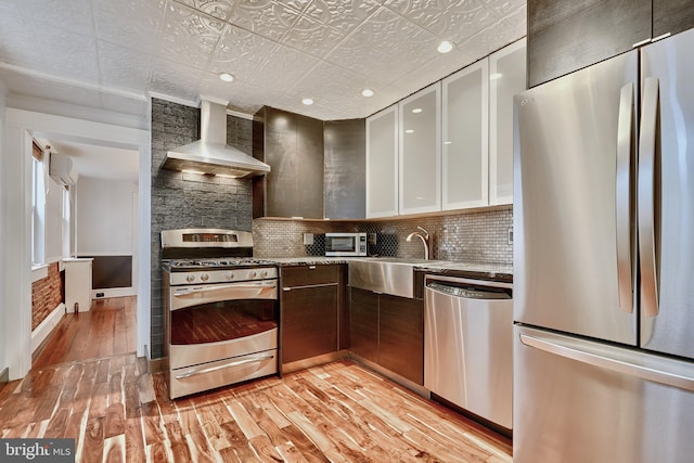 kitchen with white cabinetry, sink, appliances with stainless steel finishes, wall chimney exhaust hood, and light hardwood / wood-style flooring